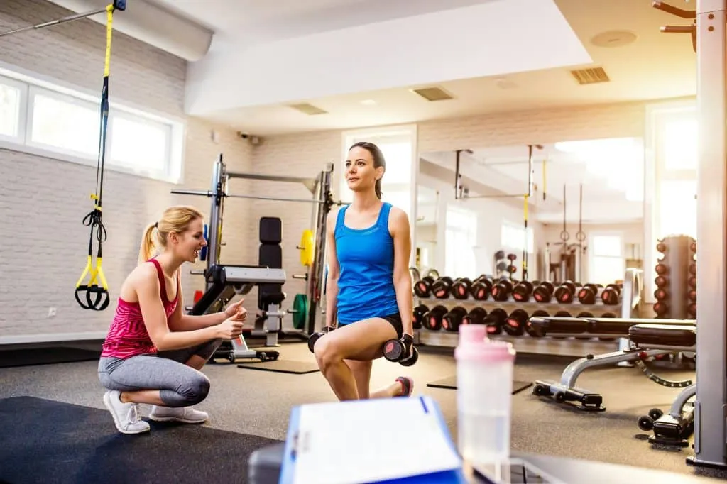 Personne effectuant une fente avec des haltères dans une salle de sport